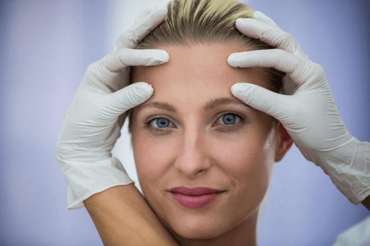 Mujer mirando a la cámara, las manos del doctor señalan su frente libre de arrugas después de usar Alluzience Botox